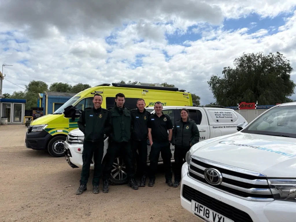 London Ambulance Service HART team smiling with Beyond Driving vehicles and yellow NHS ambulance in background