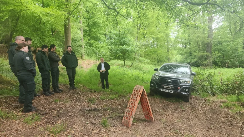 Instructor briefing NHS HART team beside Beyond Driving 4x4 training vehicle and traction boards in forest setting