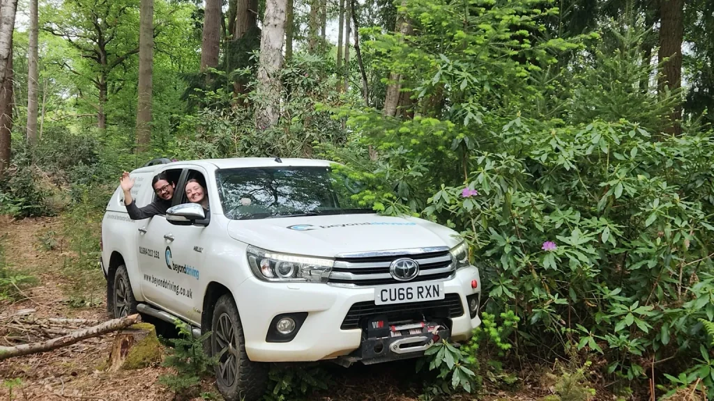 Beyond Driving trainees smiling from a white Toyota Hilux during 4x4 driver training in woodland setting