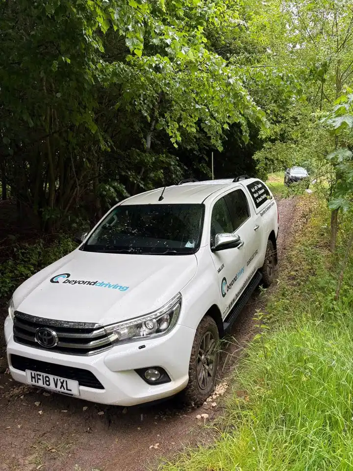 Driving Toyota Hilux descending wooded incline on off-road route during training in Lincolnshire