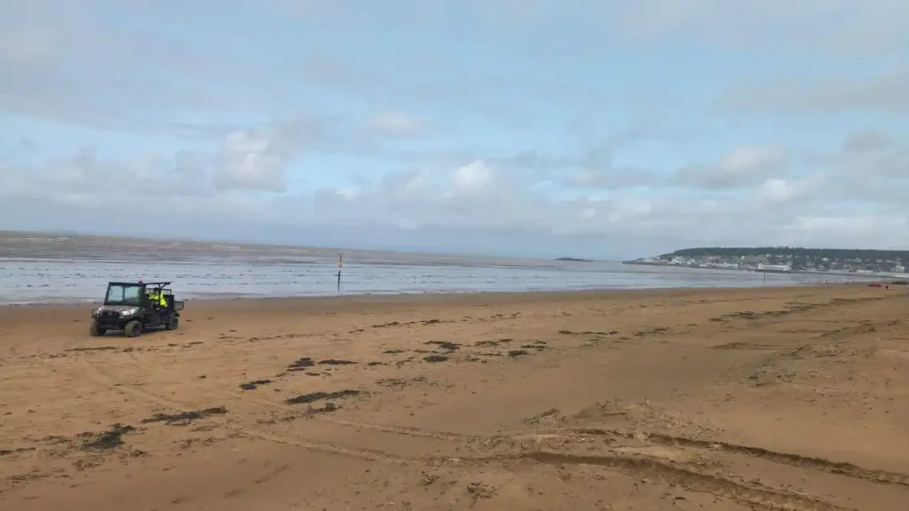A UTV driving along Weston-super-Mare beach with coastal town in the distance.
