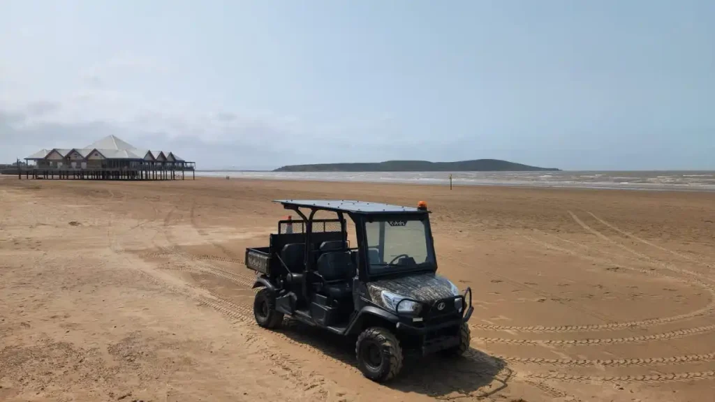 A UTV driving along Weston-super-Mare beach with coastal town in the distance.