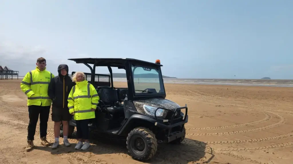 hree North Somerset Council trainees standing beside a UTV on Weston beach.