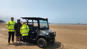 Three North Somerset Council trainees standing beside a UTV on Weston beach.