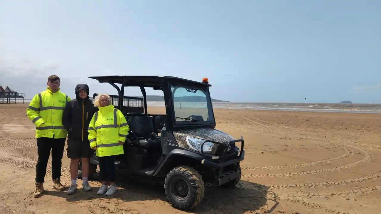 Three North Somerset Council trainees standing beside a UTV on Weston beach.