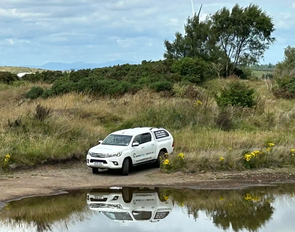 Beyond Driving 4x4 training vehicle navigating off-road terrain beside a water hazard in Fife, Scotland