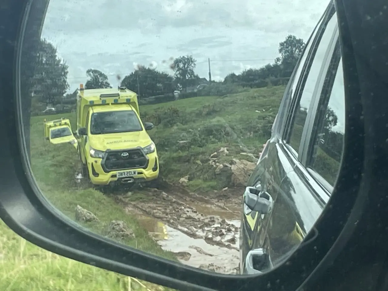 Rear-view mirror showing HART ambulances on muddy off-road track during training