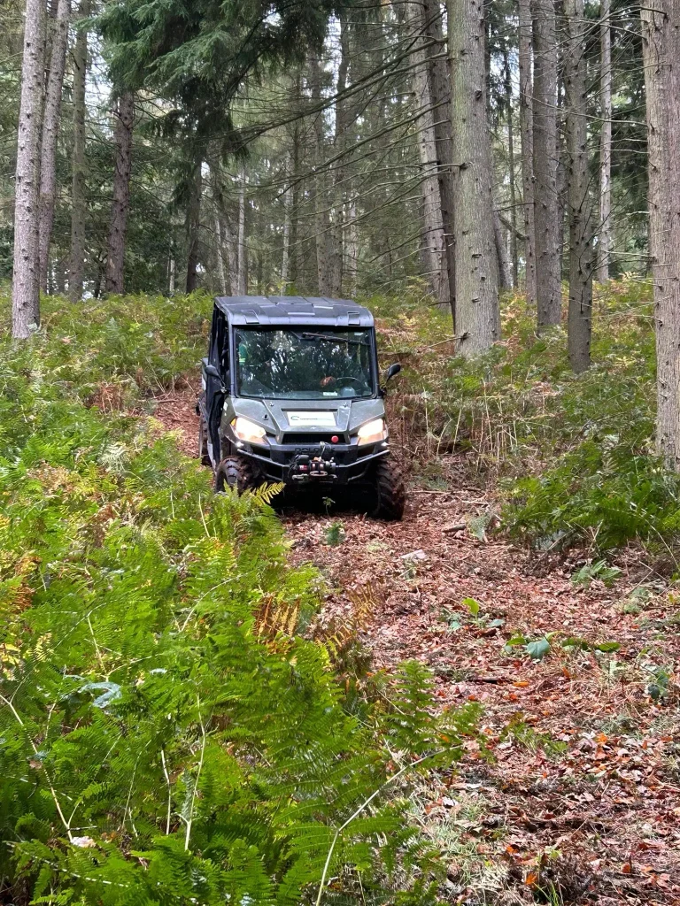 Polaris off-road utility vehicle navigating woodland terrain during Beyond Driving refresher training for London Ambulance Service HART operators.