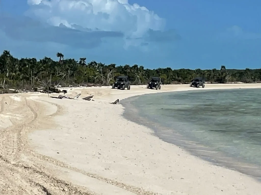 Three UTV vehicles driving along Caribbean beach during off-road training exercise