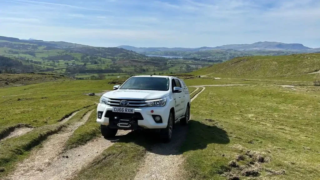 4x4 vehicle driving across open hillside terrain during training in North Wales