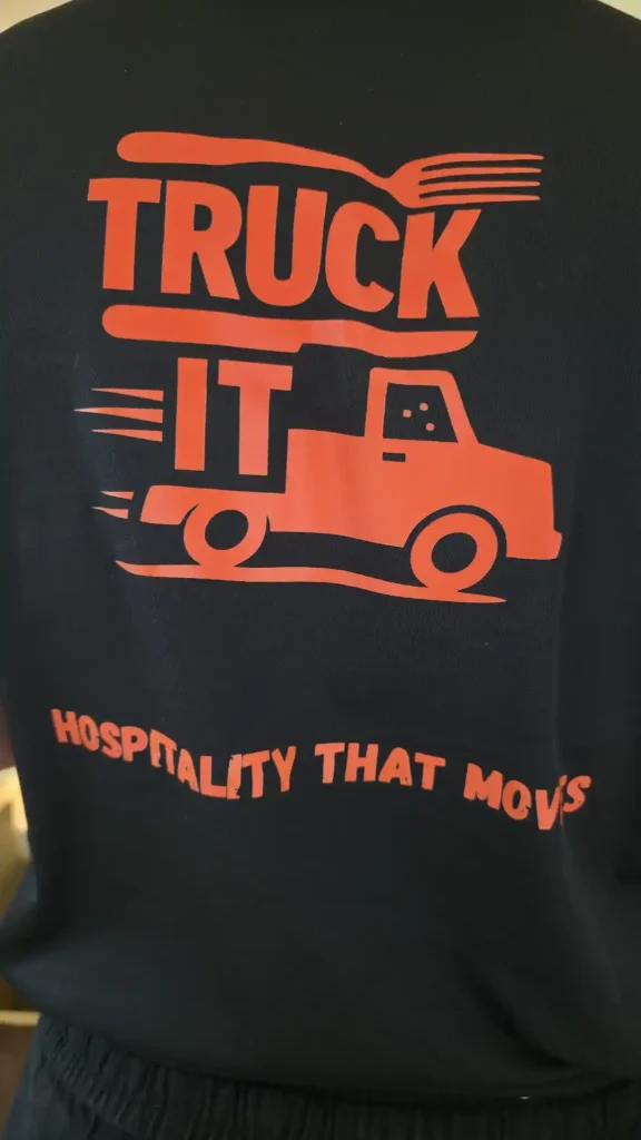Truck It branded staff shirt showing orange food truck logo and “Hospitality that moves” slogan